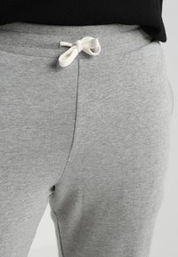 Pantalones de chándal grises con una cinturilla acanalada y cordón blanco, textura suave y detalles en las costuras laterales.