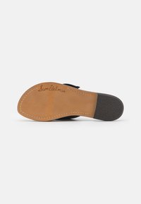 Musta sandaalin pohja, jossa on vaaleanruskea nahkainen sisäpohja. Koristeena ommeltuja yksityiskohtia ja teksturoitu musta kumipohja. Allekirjoitus "Sam Edelman" kaiverrettuna.