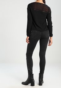 Zwarte long-sleeve top met een doorzichtige achterkant en kantdetail, gecombineerd met zwarte skinny jeans en enkellaarsjes met een blokhak.