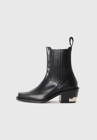 Bottine en cuir noir avec des panneaux élastiques sur les côtés, un bout pointu et un talon métallisé sculpté avec un détail ondulé. Texture lisse.