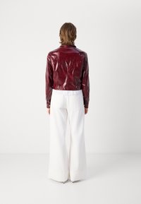 Bordowa skórzana kurtka o błyszczącym wykończeniu, krótkim kroju i spiczastym kołnierzu, zestawiona z białymi spodniami o szerokich nogawkach z teksturowanym obszyciem.