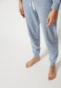 Hellblaue Sweatpants aus weichem Material mit weißem Kordelzug, versehen mit einem Stern- und Mondmuster, elastischen Bündchen und einem lässigen Schnitt.