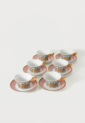 Six tasses à thé ornées avec des anses en forme d'ailes dorées et des soucoupes assorties roses et dorées, disposées en deux rangées sur une surface blanche.