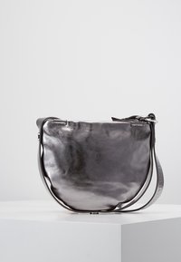 Metallinen hopeinen olkalaukku, jossa on pyöreä muoto, sileä pinta ja pitkä hihna, jossa on kohotettu brändinimi.