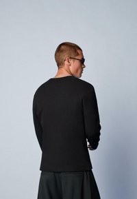 Čierna dlhá ribbovaná tričko s okrúhlym výstrihom, s textúrovanou tkaninou a rovnými strihom, nosené so tmavými nohavicami a slnečnými okuliarmi.