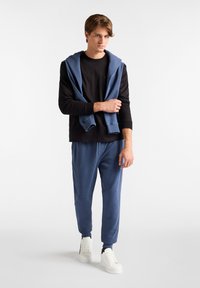 Crna majica s dugim rukavima, plavi dukserica prebačena preko ramena, plave trenirke, bijele tenisice. Mekani pamučni materijal, ležeran kroj, minimalistički dizajn.