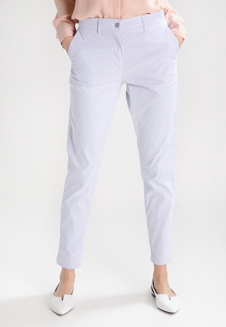 Ljusblå randiga byxor med slim fit, tillverkade av ett mjukt tyg. Har sidofickor och knäppning med knapp. Matcher med vita skor.