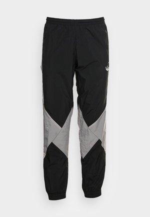 Czarno-szare spodnie dresowe Adidas z elastycznym pasem, zapinanymi na zamek kieszeniami po bokach i logo na udzie, na białym tle.