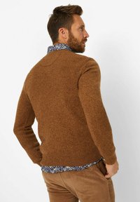Brauner, strukturierter Pullover mit gerippten Akzenten an den Schultern und Ärmeln, über einem floral gemusterten Hemd getragen. Passt gut zu slim-fit beigen Hosen.