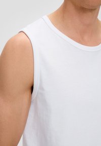 T-shirt sans manches blanc en coton doux. Présente un col rond et des bords finis avec soin. Texture lisse avec un minimum de détails.