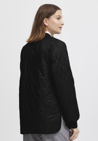Sort, kviltet lang jakke med en glat tekstur, der har en afrundet kant, ribbede manchetter og et minimalistisk design.