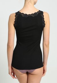 Top a canotta nero a coste con pizzo lungo il collo, forma aderente e design senza maniche. Texture morbida, adatta per essere indossata a strati.