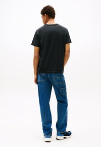 Juodas medvilninis marškinėlis derinamas su mėlynais džinsiniais kelnėmis su daugybe kišenių. Modelis dėvi baltus ir mėlynus sportbačius.