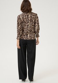 Leopard print blouse with long sleeves, gathered cuffs, and a relaxed fit, paired with black wide-leg trousers and heels.