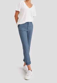 Blå bomullsbukser med uppvikta fållar, kombinerade med en vit V-hals T-shirt och vita sneakers. Enkelt mönster, mjuk textur, avslappnad passform.