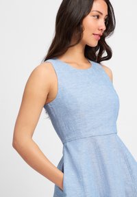 Lichtblauwe mouwloze jurk met een getailleerde bovenkant, uitlopende rok en zijzakken; gemaakt van een gestructureerde stof met een gladde afwerking.