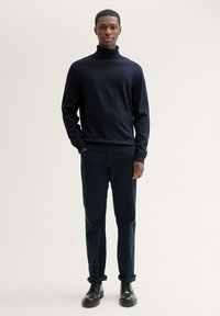 Granatowy sweter z golfem wykonany z dzianiny, zestawiony z ciemnymi spodniami i czarnymi sznurowanymi butami. Prosty, dopasowany krój z prążkowanymi mankietami.