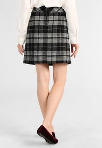 Jupe à carreaux noir et gris avec une taille ajustée et une fermeture éclair à l'arrière. Présente une silhouette évasée et une texture douce.