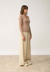 Cardigan ajustado color marrón claro con cierre de cremallera, combinado con pantalones de pierna ancha de canalé color crema y zapatillas ligeras. Textura de tela suave.