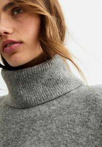 Grijze coltrui van zacht brei-jacquard met ribbeltextuur. Close-up focust op de kraag en het schoudergebied.
