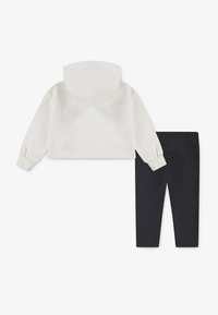Hvit cropphettegenser med hette og ribbede mansjetter, kombinert med svarte leggings, som har en glatt tekstur og en tettsittende design.