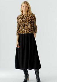 Luipaardprint sweater gemaakt van zachte stof, gecombineerd met een vloeiende zwarte maxi rok. De outfit wordt aangevuld met zwarte laarzen tot de knie.