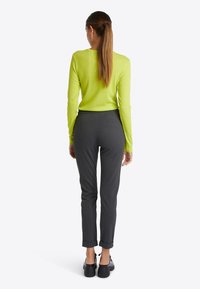 Ljus limegrön långärmad topp med anpassad passform, i kombination med mörkgrå tapered byxor med uppvikta ärmar och svarta skor. Slät textur.