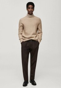 Pull à col roulé beige à côtes associé à un pantalon marron bien taillé et des chaussures noires. La coupe est décontractée avec un motif tricoté texturé.