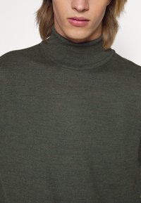 Grønn genser med høy hals, strikket tekstur, tettsittende design, ribbestrikket hals, glatt stoff med subtile variasjoner i fargen.