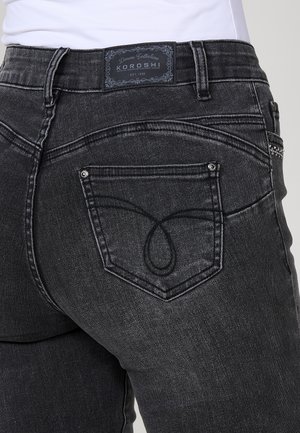 Pantalones vaqueros de mezclilla negra con una cintura de altura media, bolsillo trasero con costura decorativa y una etiqueta de marca en la cinturilla.