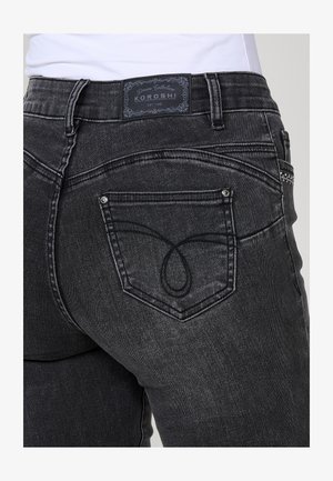 Melna džinsu auduma bikses ar vidēja pacēluma jostasvietu, aizmugurējo kabatu ar dekoratīvu izšuvumu un zīmola etiķeti jostas vietā.