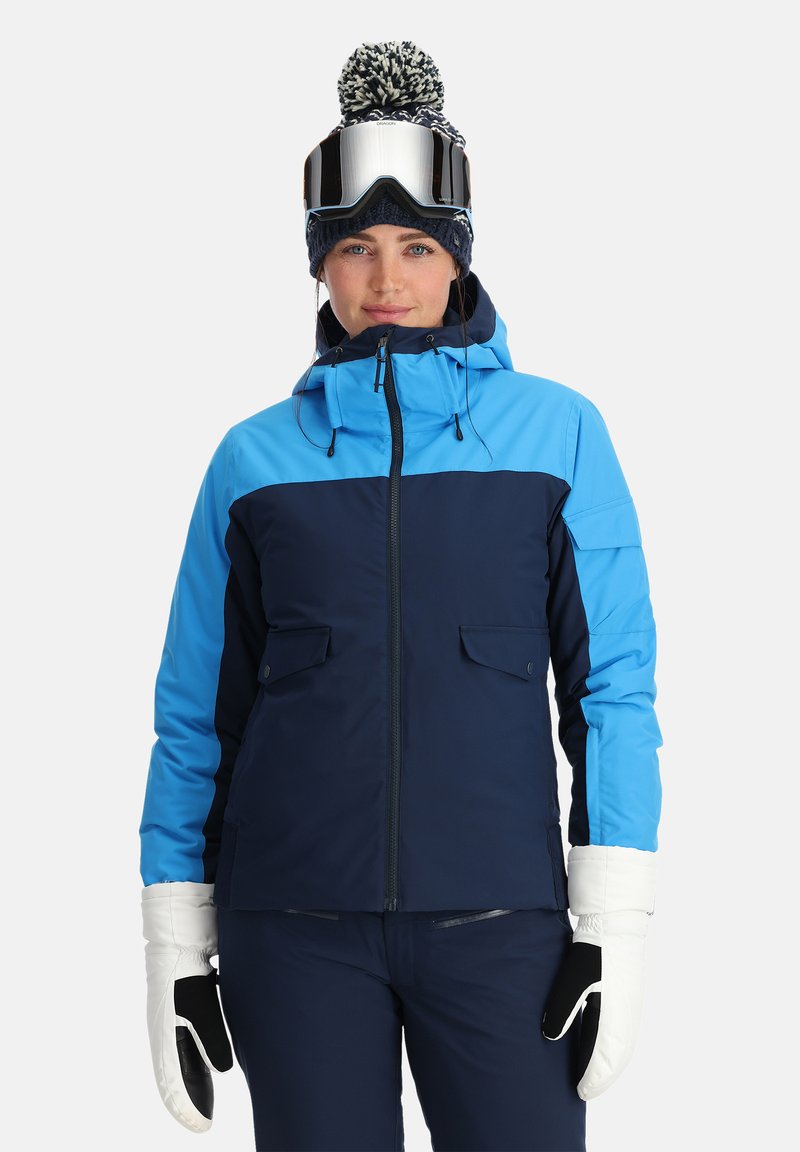 Skijacke im blau und navy Farbblock-Design, mit Kapuze, frontalen Taschen und kombiniert mit weißen Handschuhen und Skibrille.