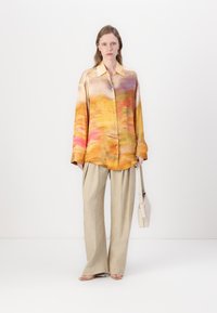 Silk blouse with a gradient pattern of orange, pink, and yellow tones; features a collar and button front. Paired with beige wide-leg trousers.