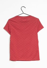 Röd bomulls t-shirt med rund hals, korta ärmar och ett mönster av små vita prickar över hela. Hänger från en svart krok.