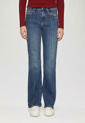 Blue denim flared jeans with front seam detailing, two front pockets, and a standard waistband. Paired with white sneakers.