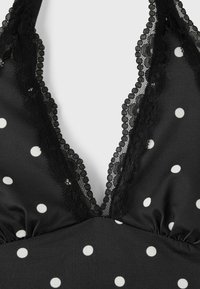 Tissu noir à pois blancs avec une bordure en dentelle noire le long d'un décolleté en V profond.