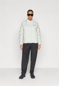 Lys grå quiltet pufferjakke med krave og logo, parret med sorte cargo bukser og sorte sneakers, med en glat tekstur.