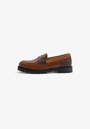 Mocassin en cuir marron avec un détail de bride plus foncé, semelle épaisse noire à crampons et finitions cousues, présenté de côté sur fond blanc.