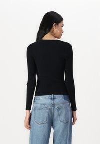 Black ribbed long-sleeve top features a fitted design. Paired with high-waisted light blue denim jeans, visible back pockets and stitching details.