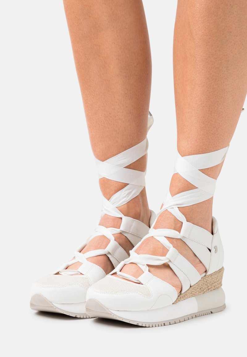 Sandalias de cuña blancas con correas de tobillo entrelazadas, parte superior texturizada y suela de mimbre. Presentan punta abierta y acentos en beige contrastantes.