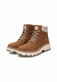 Stivali ankle in suede marrone con lacci, colletto imbottito e suola in gomma bianca con battistrada resistente per una buona aderenza. Dettaglio con zip sul lato.
