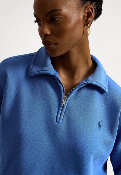 Πουλόβερ με φερμουάρ έως τη μέση σε μπλε βαμβάκι, με υφασμάτινη υφή, γιακά που διπλώνει και μικρό κεντημένο λογότυπο στο στήθος.