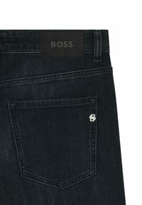 Granatowe dżinsy z ciemnego denimu z czarną skórzaną naszywką w talii z logo "BOSS", srebrnymi akcentami na tylnej kieszeni oraz klasycznym designem.