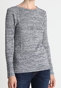 Šedý pletený top s dlouhým rukávem a texturovaným vzorem. Kulatý výstřih a přiléhavé rukávy, kombinované s tmavými džíny. Měkká, pohodlná tkanina.