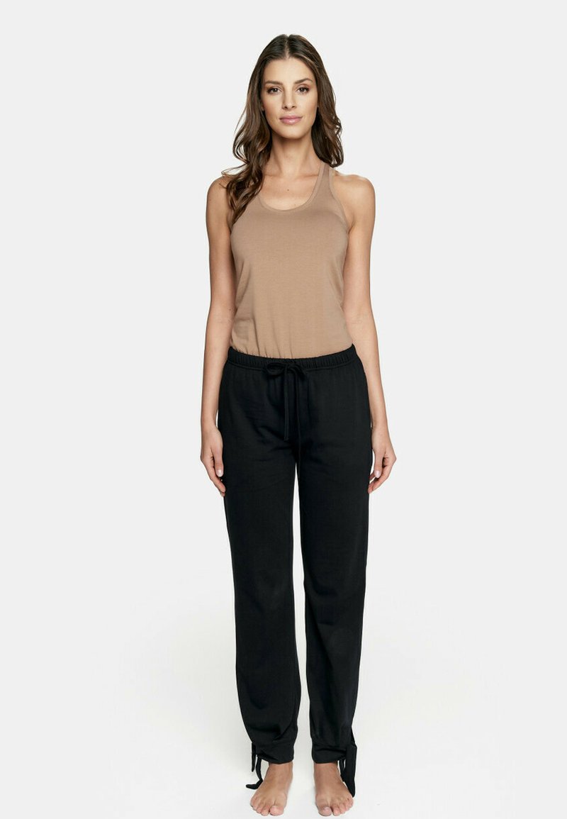 Beżowa bluzka na ramiączkach z cienkimi szelkami zestawiona z czarnymi, luźnymi spodniami z elastycznym pasem i wiązaniami przy kostkach.