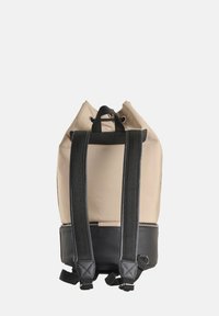 Mochila de tela beige con base de cuero negro, correas ajustables negras y un cierre de cordón en la parte superior. Material duradero, diseño minimalista.