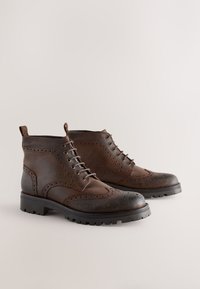Braune Leder-Stiefeletten mit Brogue-Details, Schnürdesign, abgerundetem Zehenbereich und dicker Gummisohle mit grobem Profil.