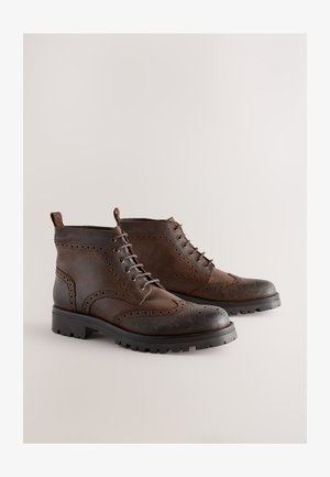 Braune Leder-Stiefeletten mit Brogue-Details, Schnürdesign, abgerundetem Zehenbereich und dicker Gummisohle mit grobem Profil.