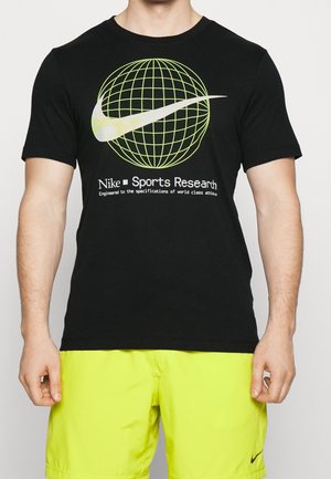 Mężczyzna w czarnej koszulce Nike z zielonym globem i logo Swoosh, w połączeniu z neonowożółtymi szortami Nike.