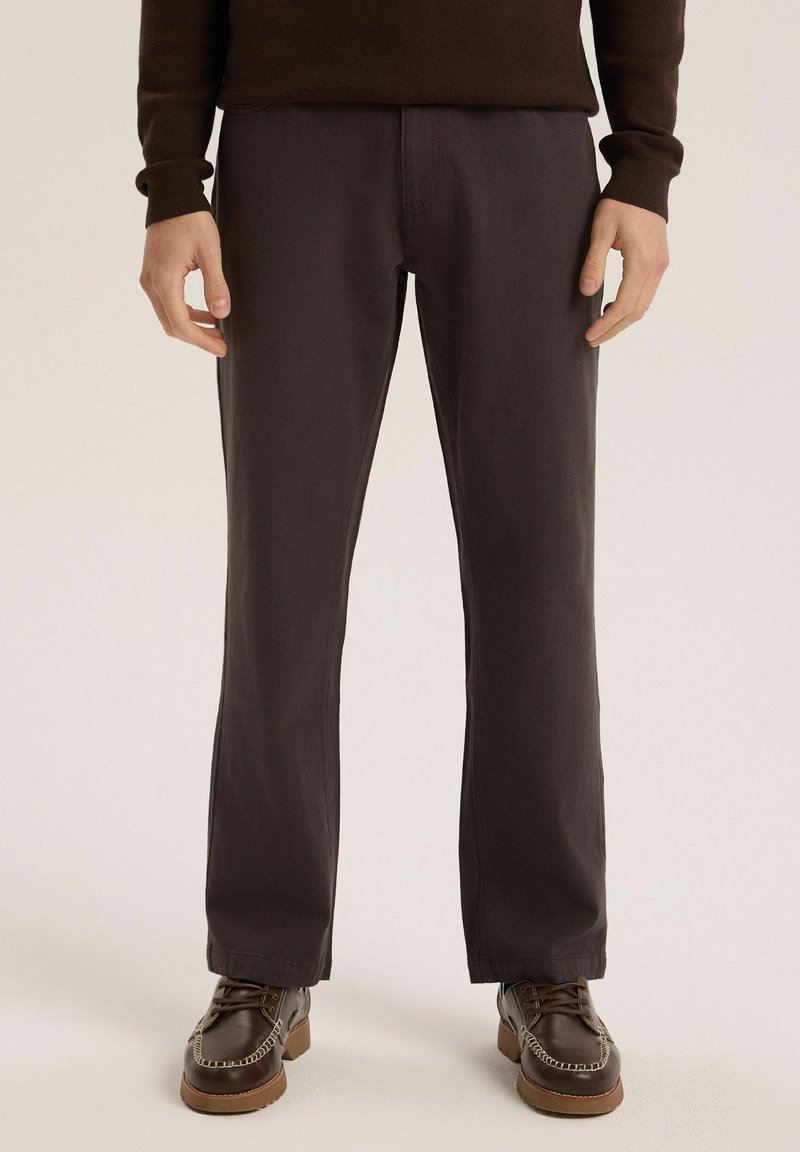 Ciemnoszare bawełniane spodnie o prostym kroju. Noszone z brązowymi skórzanymi butami, ozdobione dekoracyjnym przeszyciem.